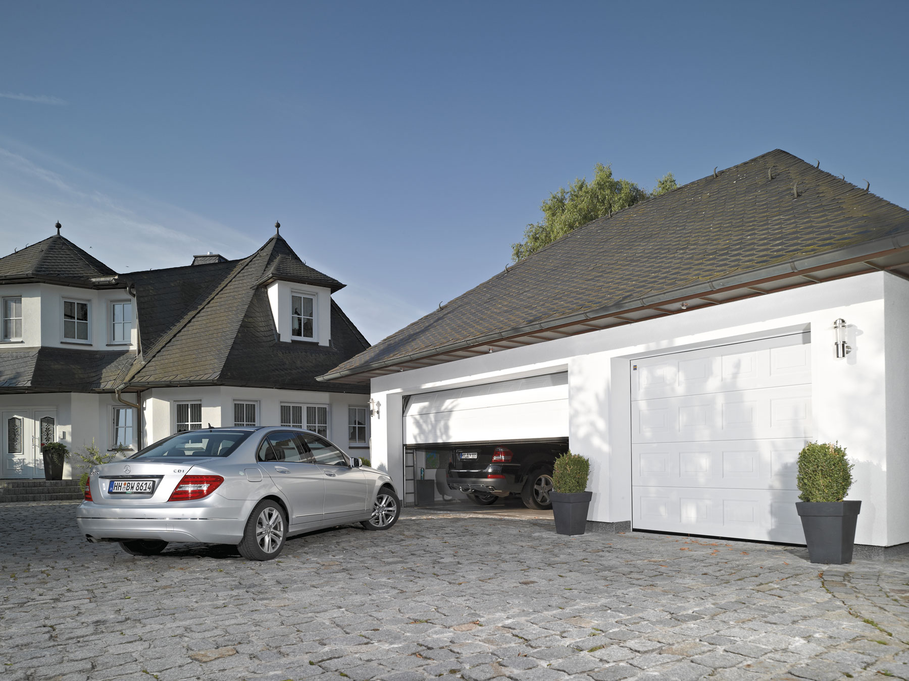 Zwei graue Garagentore, in einem steht ein Auto und ein anderes Parkt davor.