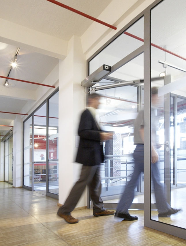 Menschen laufen durch eine geöffnete Tür, die durch einen Drehflügelantrieb geöffnet wurde.